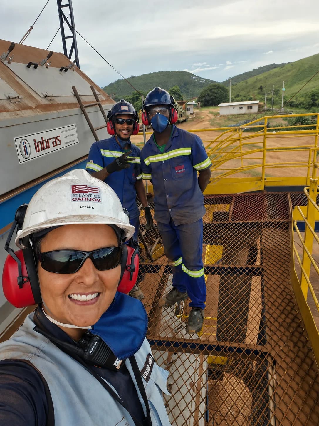 Três integrantes da equipe da Mina Carijós, com capacete, óculos e protetor auricular, na passarela metálica da usina