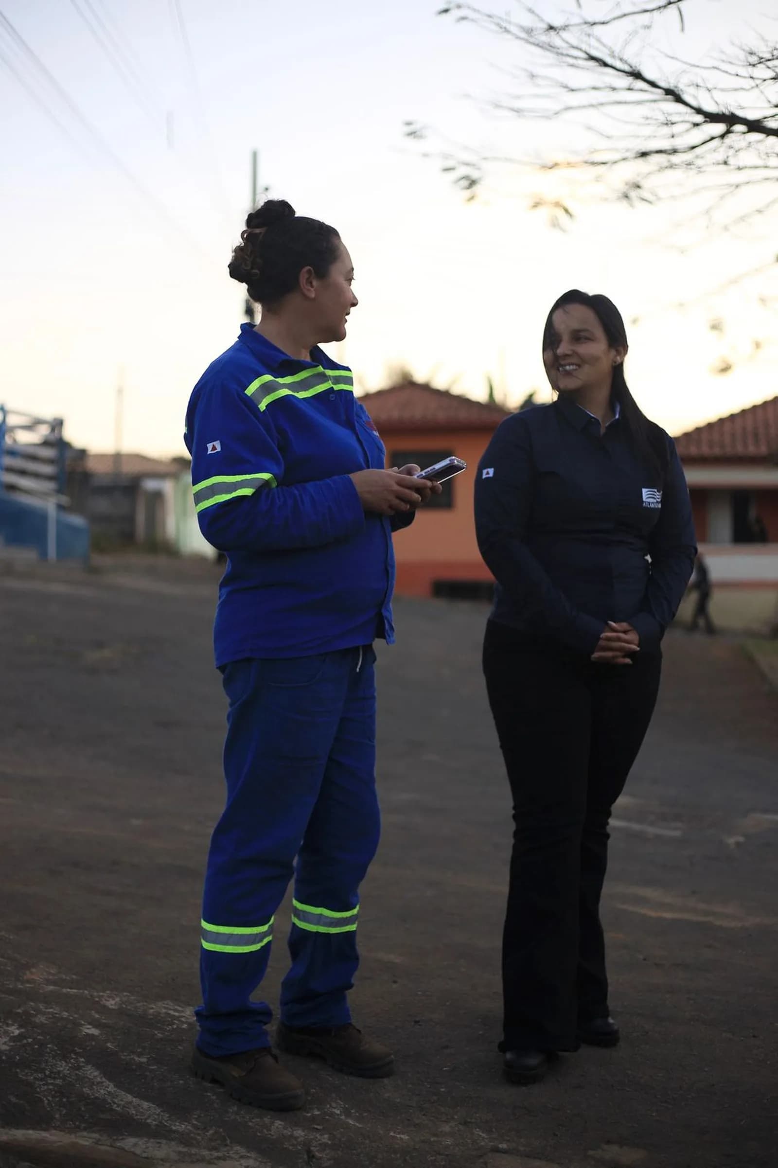 Duas integrantes da equipe conversam ao ar livre, no fim da tarde, na área da operação