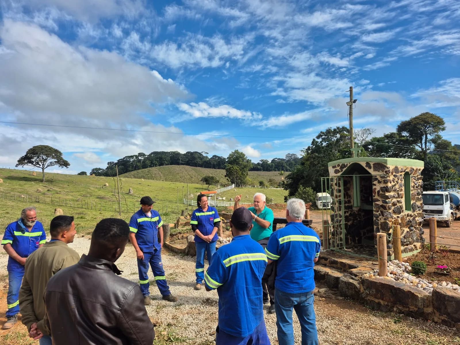 Equipe reunida em semicírculo ao ar livre, diante do oratório de pedra, durante uma conversa em grupo