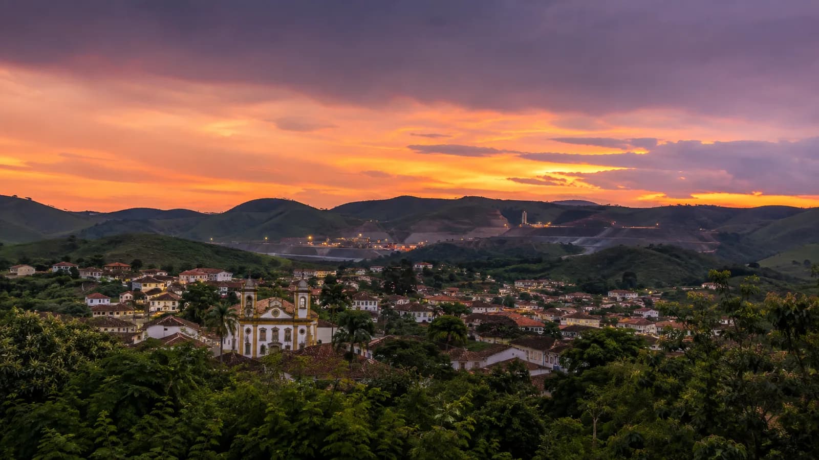 Cidade histórica mineira ao anoitecer, entre morros.
